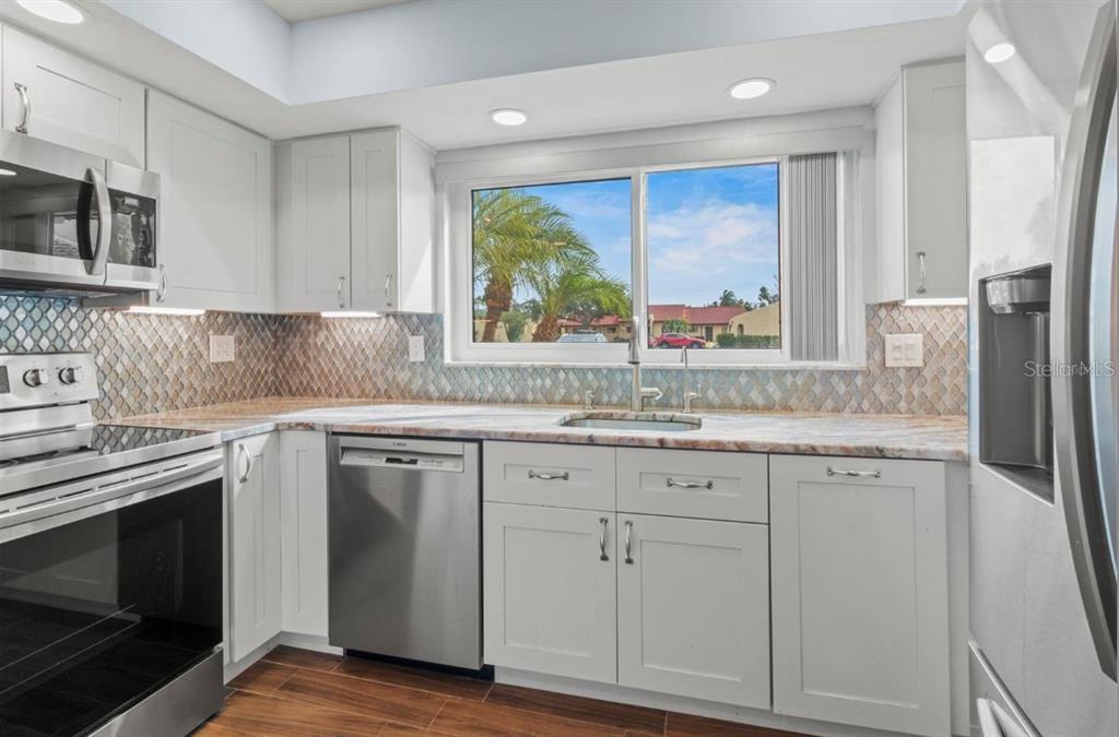 A kitchen with white cabinets, stainless steel appliances, a patterned backsplash, and a window view — 1446 56TH STREET W UNIT #1446, BRADENTON, FL