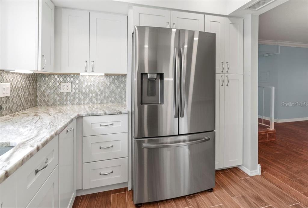 A kitchen features white cabinets, a stainless steel refrigerator, and a patterned tile backsplash — 1446 56TH STREET W UNIT #1446, BRADENTON, FL