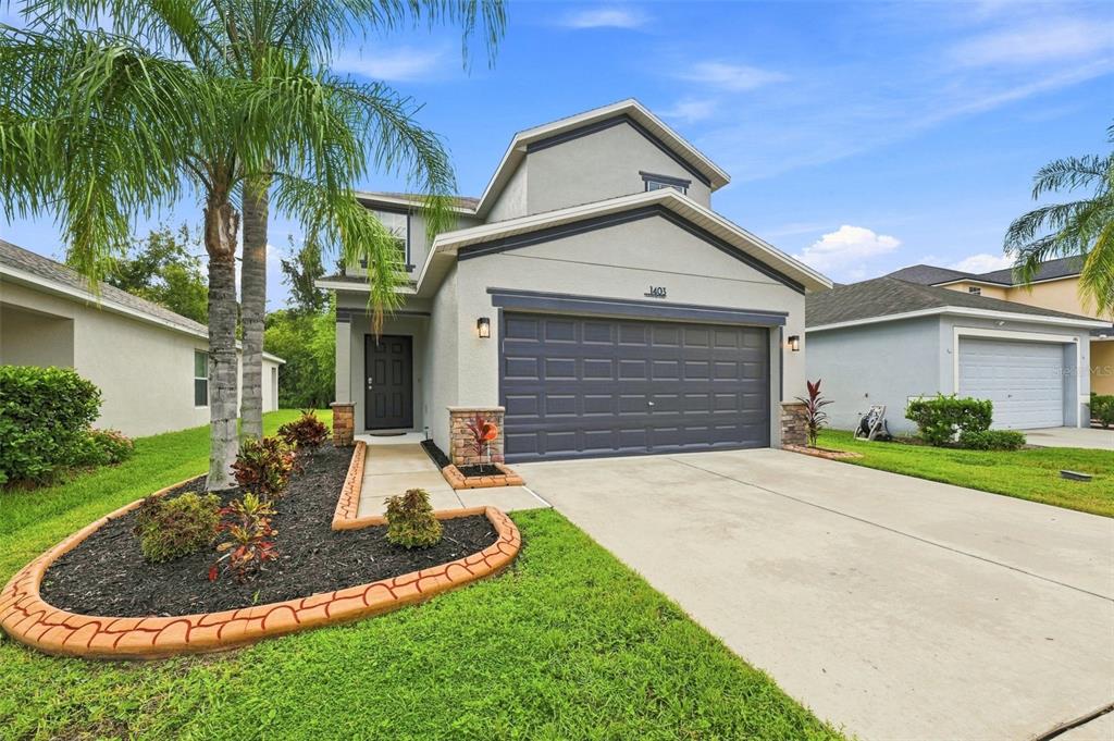A two-story house with a gray exterior, a dark garage door, and a landscaped front yard — 1403 TRAILWATER STREET, RUSKIN, FL
