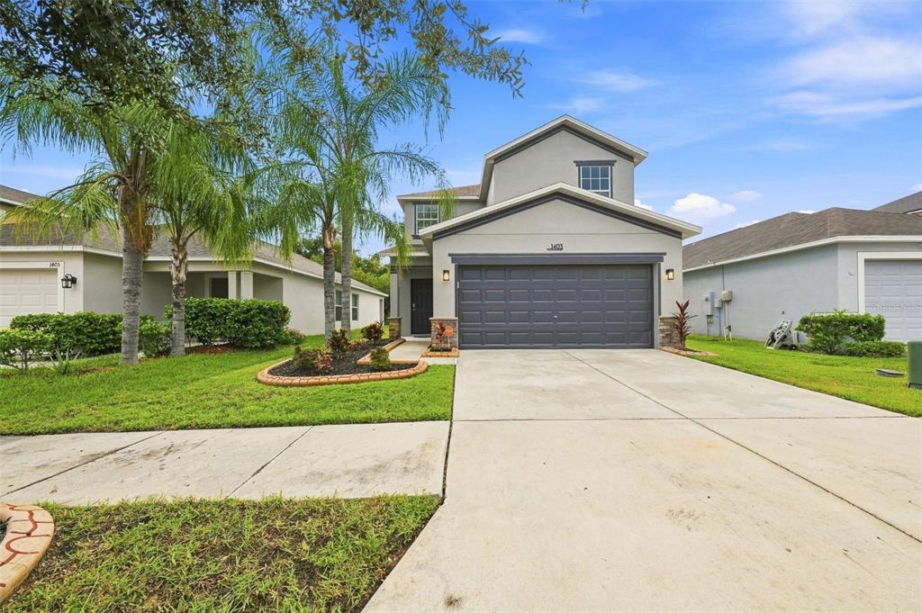 A two-story suburban house with a gray exterior, a dark garage door, and a concrete driveway — 1403 TRAILWATER STREET, RUSKIN, FL