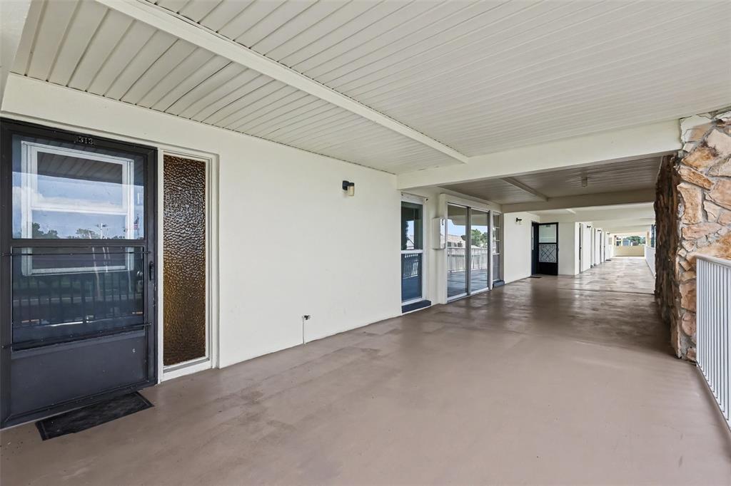 A covered outdoor walkway features a concrete floor, white walls, and a stone accent wall — 6100 12TH STREET S UNIT 313, ST PETERSBURG, FL