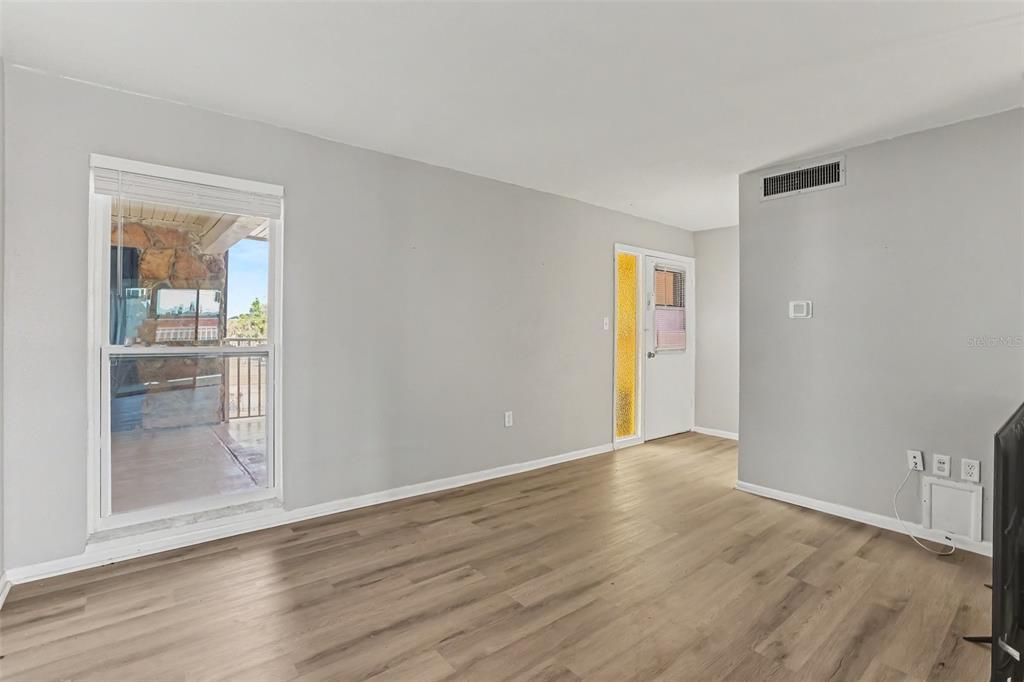 A living room with light gray walls, wood-look flooring, and a view of a patio — 6100 12TH STREET S UNIT 313, ST PETERSBURG, FL