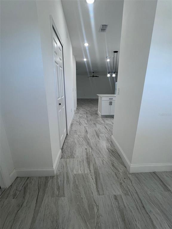 A hallway with gray wood-look tile flooring leads to a kitchen with white cabinets — 2281 WHITLEY LANE, WINTER HAVEN, FL
