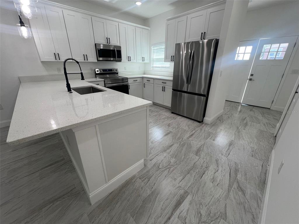 A modern kitchen features white cabinets, quartz countertops, stainless steel appliances, and gray tile flooring — 2281 WHITLEY LANE, WINTER HAVEN, FL