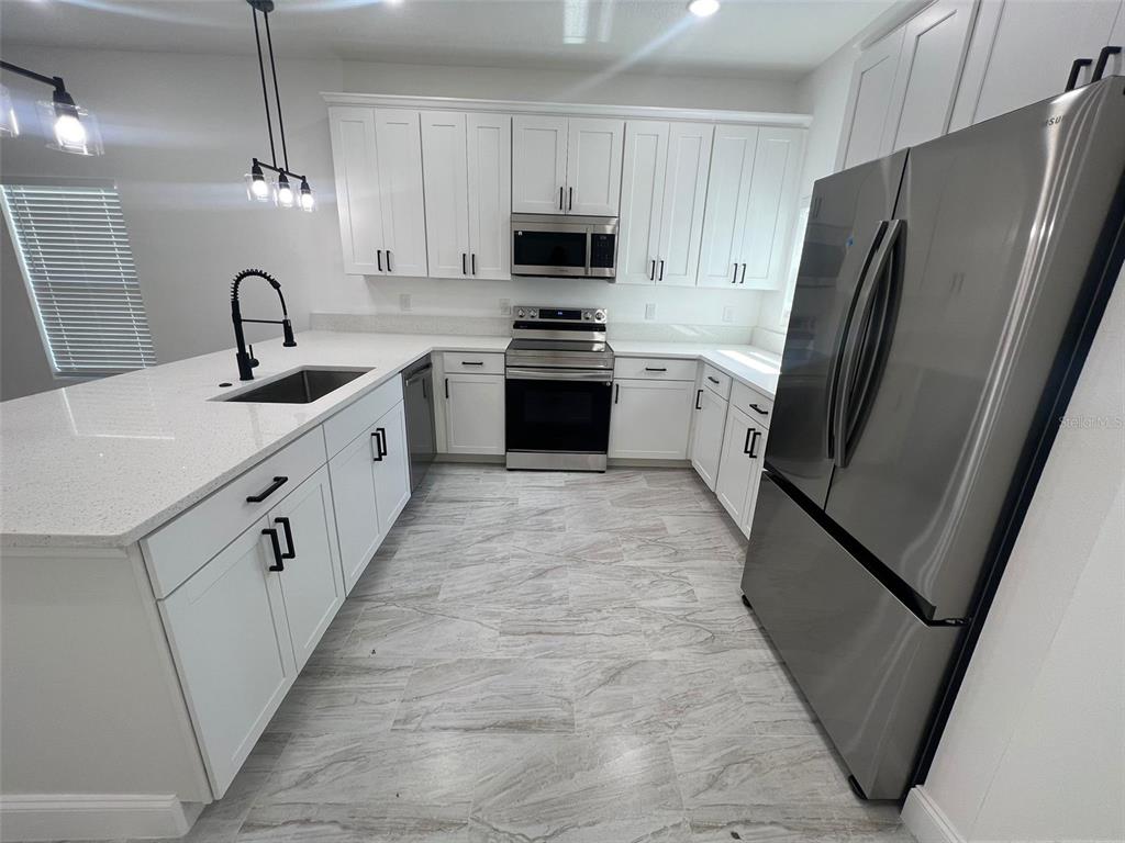 A modern kitchen features white cabinets, stainless steel appliances, and a large quartz-topped island — 2281 WHITLEY LANE, WINTER HAVEN, FL