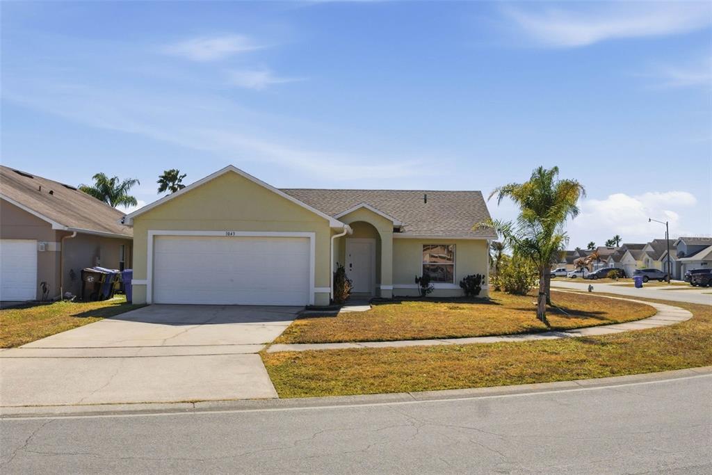A single-story house with a two-car garage, light yellow siding, and a palm tree — 1043 SOARING EAGLE LANE, KISSIMMEE, FL