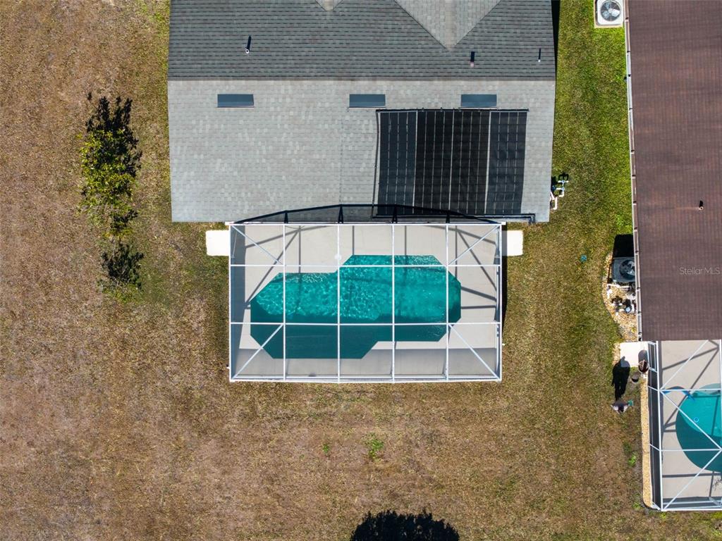 An aerial view shows a house with a solar-heated pool enclosed by a screened lanai — 1043 SOARING EAGLE LANE, KISSIMMEE, FL