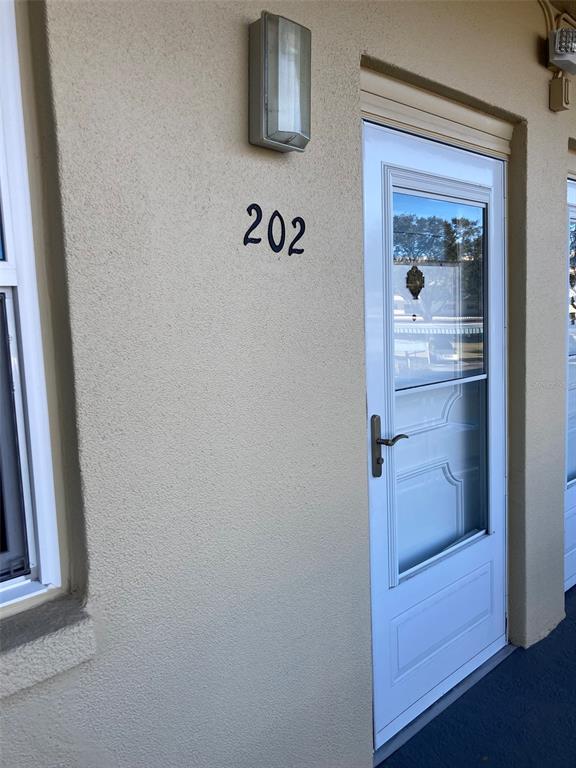 A tan exterior wall features a white door with a storm door and number 202 — 5750 80TH STREET N UNIT C202, ST PETERSBURG, FL