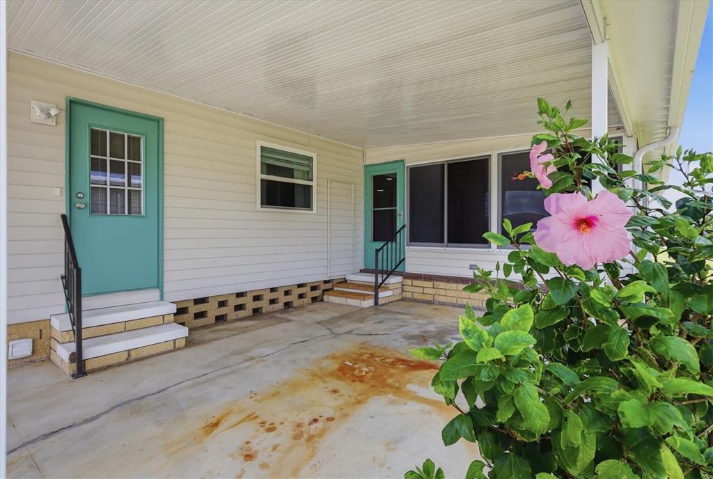 A covered concrete patio features two teal doors with steps and a large hibiscus plant — 4308 13TH STREET E, ELLENTON, FL