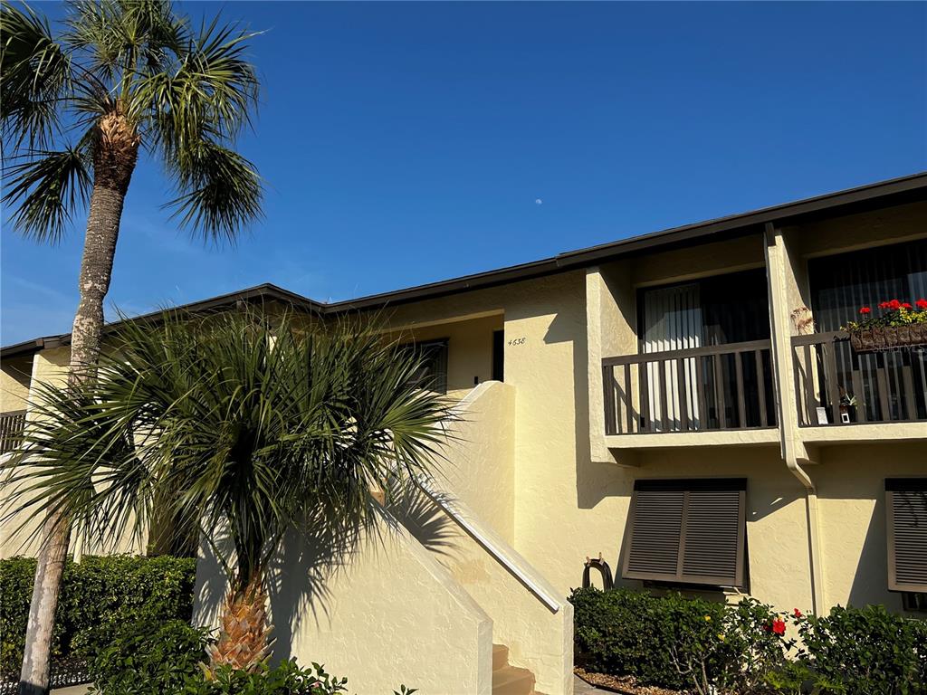 A two-story yellow stucco building features a palm tree, a balcony, and exterior stairs — 4638 LONGWATER CHASE UNIT 94, SARASOTA, FL