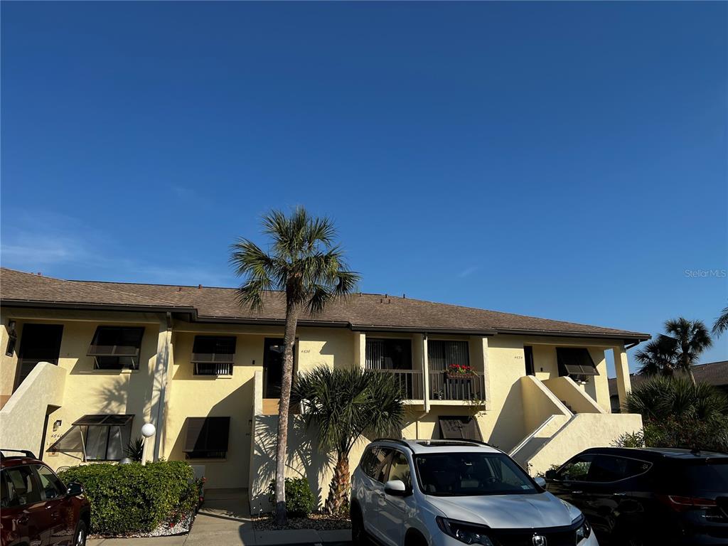 A two-story apartment building with yellow stucco walls, brown shingled roof, and parked cars — 4638 LONGWATER CHASE UNIT 94, SARASOTA, FL