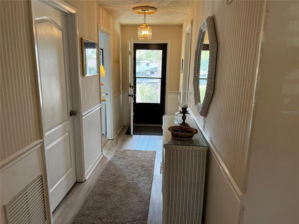 A hallway features light-colored striped wallpaper, a white console table, a mirror, and a door — 4638 LONGWATER CHASE UNIT 94, SARASOTA, FL