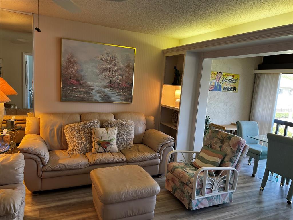 A living room features a beige leather sofa, a floral armchair, and a Yuengling beer sign — 4638 LONGWATER CHASE UNIT 94, SARASOTA, FL