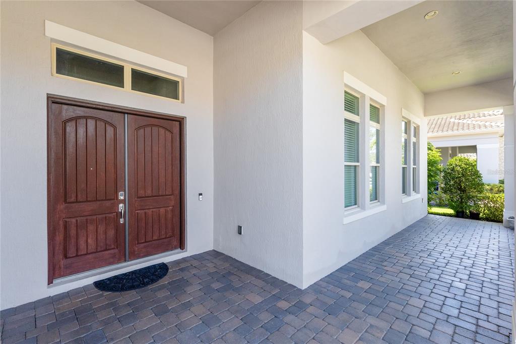 A covered entryway features a double wood door, light-colored stucco walls, and brick paver flooring — 13167 ALDERLEY DRIVE, ORLANDO, FL