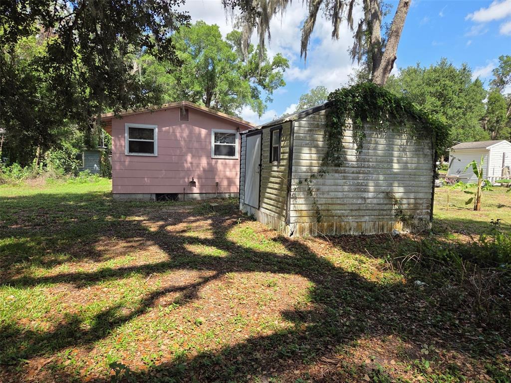 A pink house and a weathered storage shed sit on a grassy, tree-shaded lot — 4534 SEABERG ROAD, ZEPHYRHILLS, FL