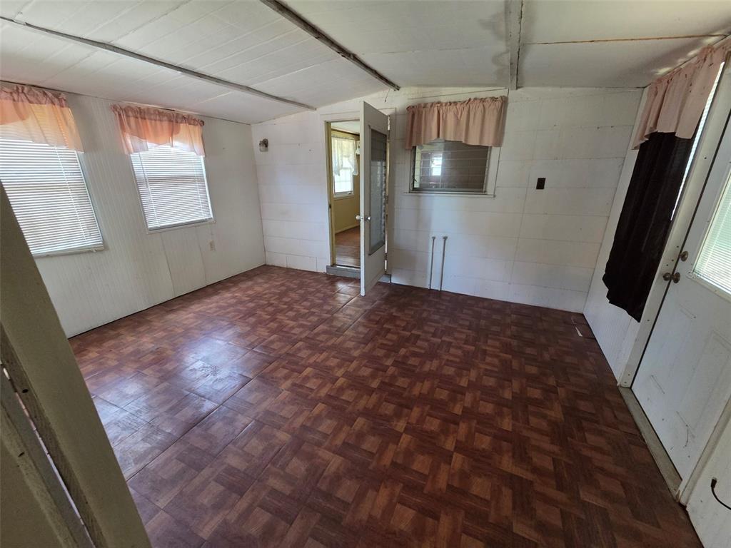 A room with wood-patterned tile flooring, white paneled walls, and several windows with pink valances — 4534 SEABERG ROAD, ZEPHYRHILLS, FL