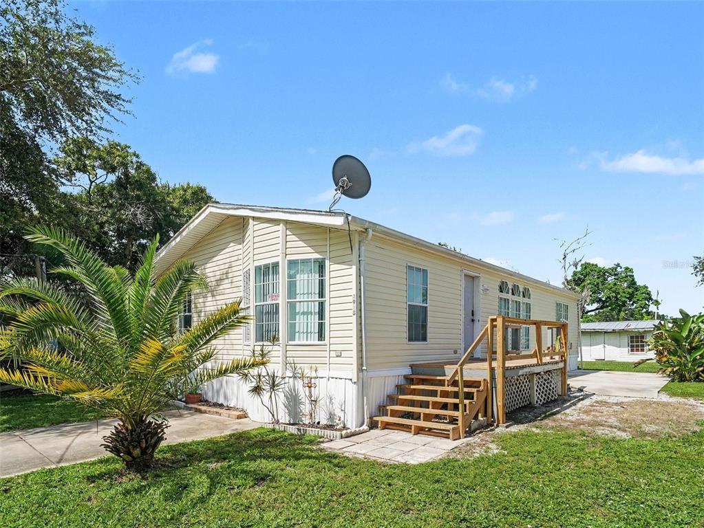 A single-story mobile home with light yellow siding, a wooden deck, and a satellite dish — 4928 ELIZABETH AVENUE, SARASOTA, FL