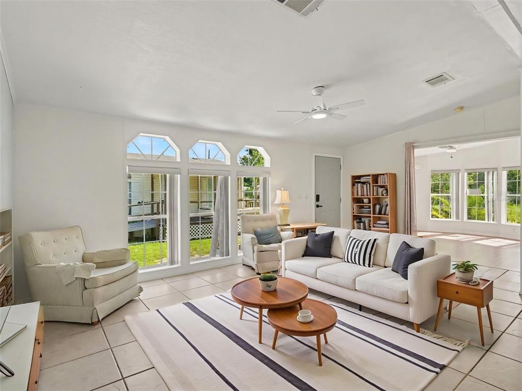 A bright living room features white walls, tile flooring, a striped rug, and large windows — 4928 ELIZABETH AVENUE, SARASOTA, FL