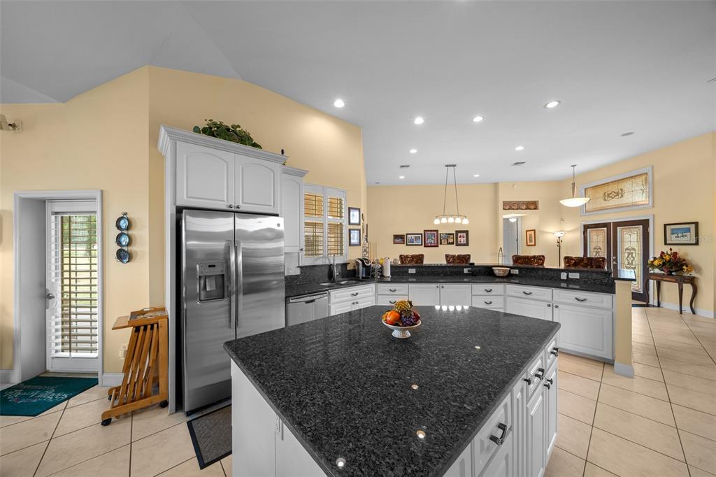 A kitchen features white cabinetry, dark granite countertops, a central island, and light tile flooring — 5170 SE HIGHWAY 42, SUMMERFIELD, FL