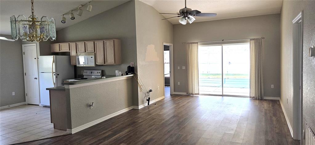 An open-concept living area features wood-look flooring, a kitchen with light cabinets, and sliding glass doors — 528 RESERVE DRIVE, DAVENPORT, FL