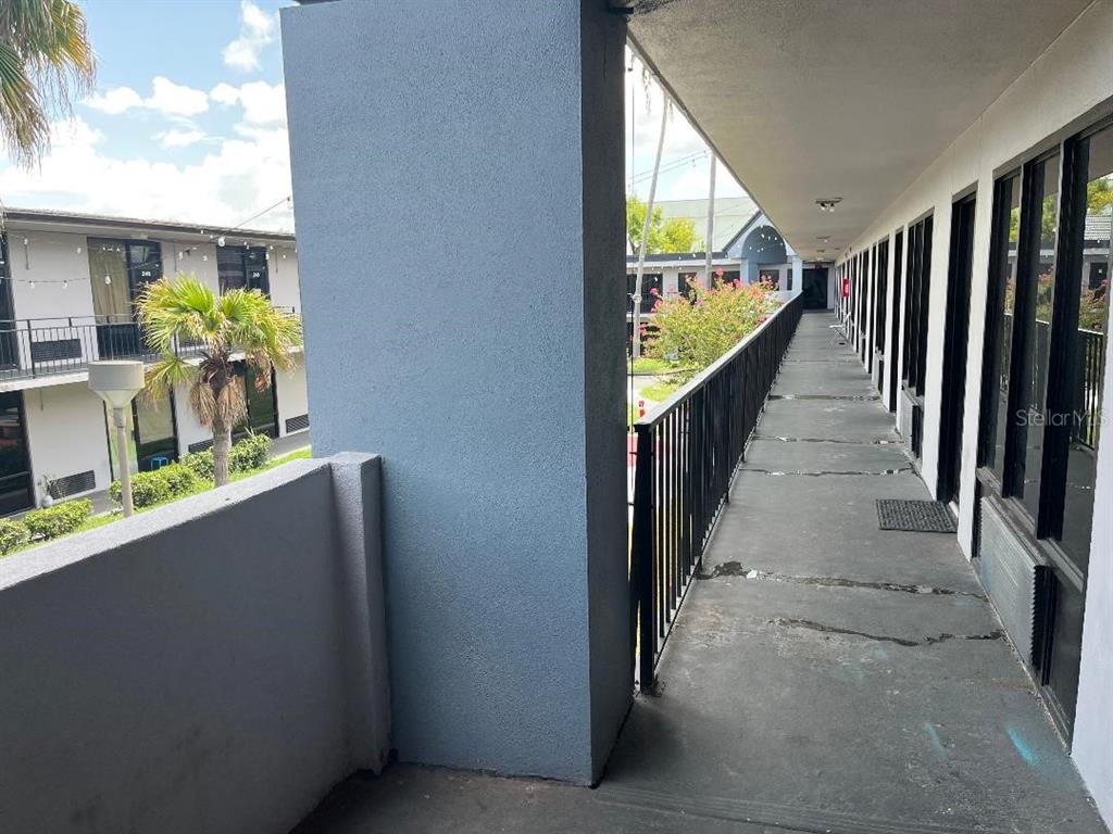 An outdoor apartment walkway with a concrete floor, metal railing, and views of other units — 8421 S ORANGE BLOSSOM TRAIL UNIT 302, ORLANDO, FL