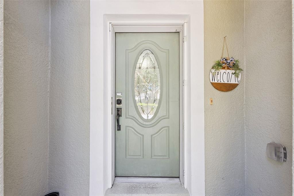 A light green front door with an oval glass insert features a hanging welcome sign — 6220 BELDON DR, MOUNT DORA, FL