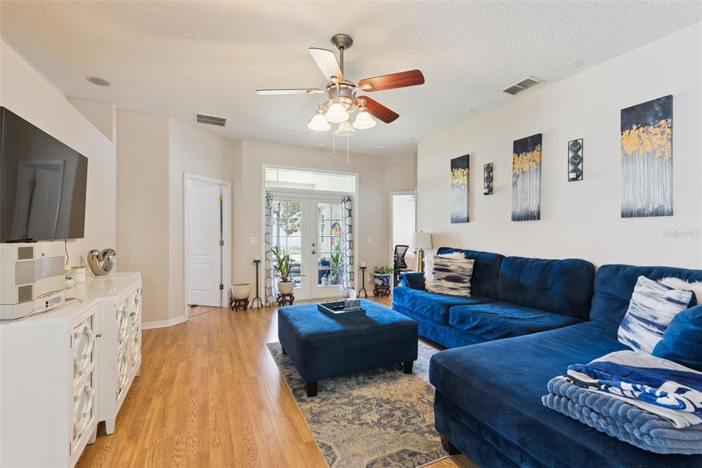 A living room features a blue sectional sofa, a matching ottoman, and wood-look flooring — 6220 BELDON DR, MOUNT DORA, FL