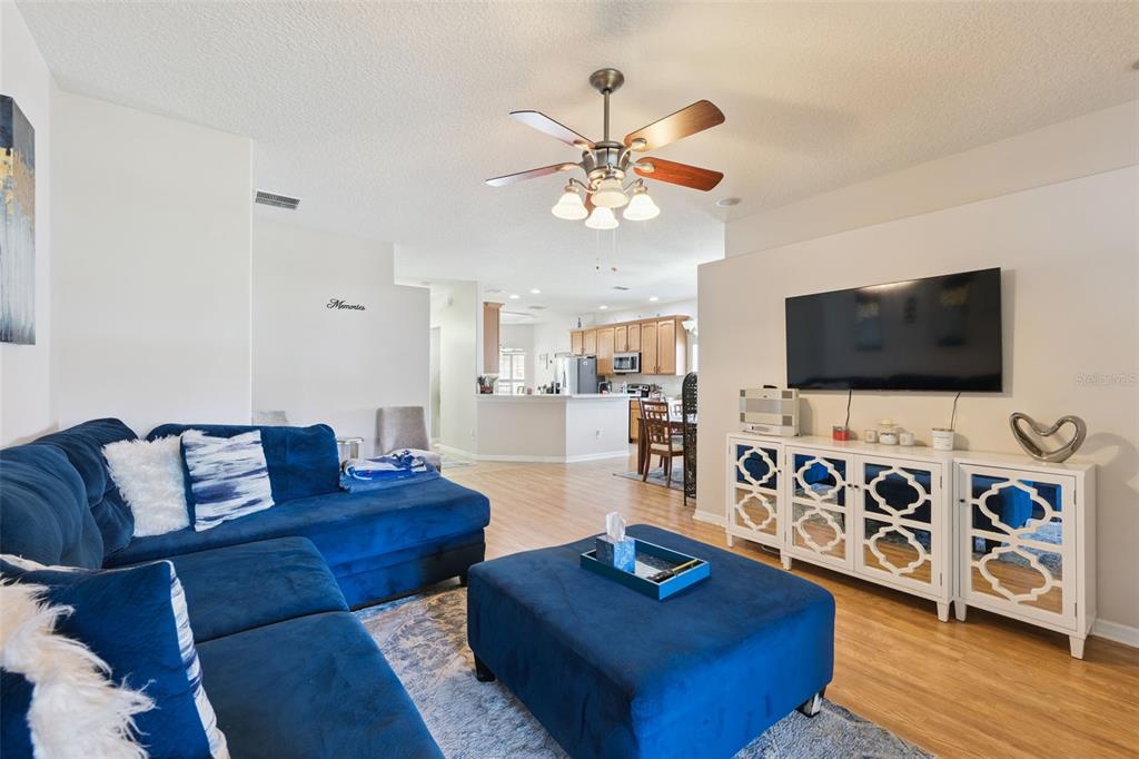 A living room with a blue sectional sofa, matching ottoman, and a wall-mounted television — 6220 BELDON DR, MOUNT DORA, FL