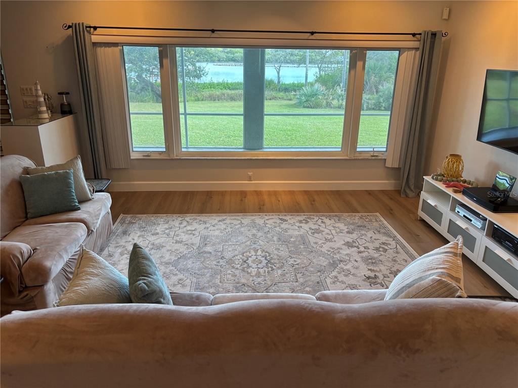 A living room features a large window overlooking a yard and water, wood flooring, and furniture — 2437 SWORDFISH LANE, EDGEWATER, FL