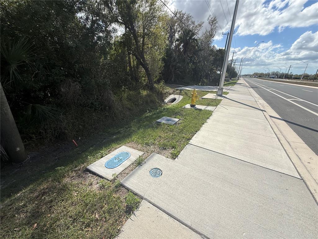 A sidewalk runs alongside a road with utility covers, a fire hydrant, and a drainage pipe — 11959 MOCCASIN WALLOW ROAD, PARRISH, FL