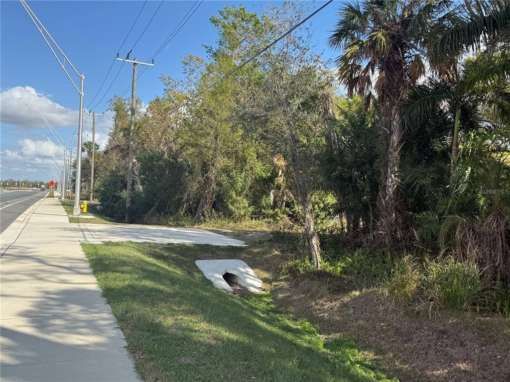 A concrete sidewalk runs alongside a road next to a grassy area with a culvert — 11959 MOCCASIN WALLOW ROAD, PARRISH, FL