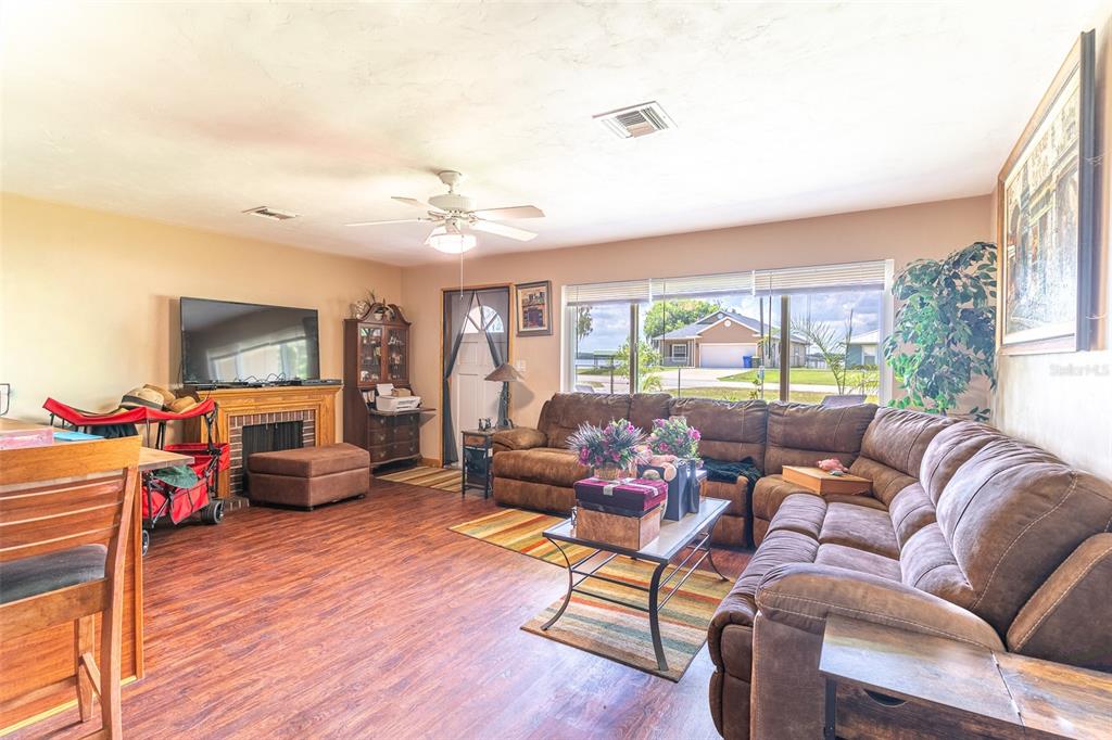 A living room features wood-look flooring, a brown sectional sofa, a fireplace, and large windows — 305 CLOVERLEAF ROAD, LAKE PLACID, FL