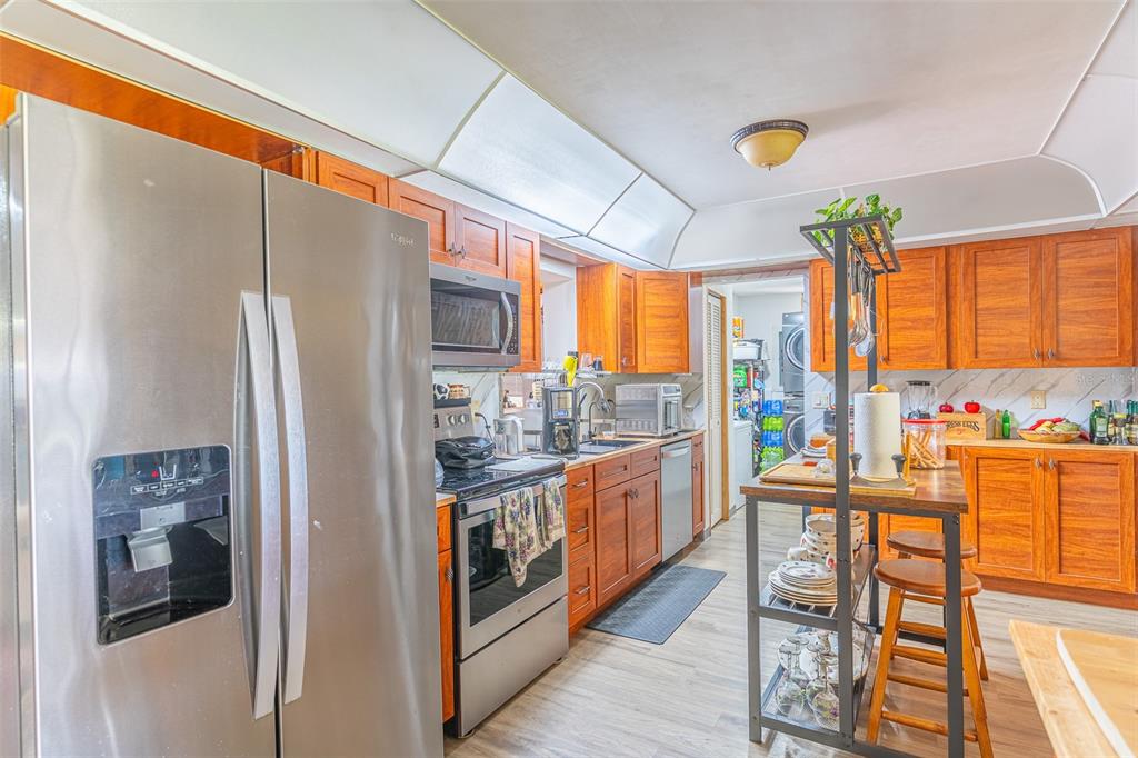 A kitchen features stainless steel appliances, wood cabinets, and a central island with bar stools — 305 CLOVERLEAF ROAD, LAKE PLACID, FL