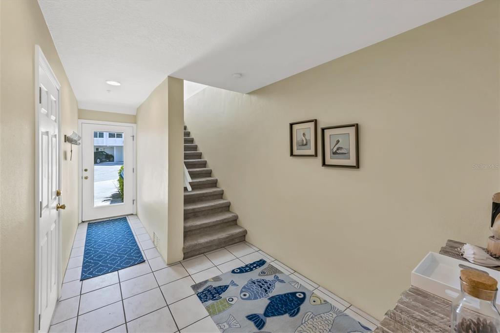 An entryway features white tile flooring, a carpeted staircase, and a glass-paneled front door — 8272 HARBORSIDE CIRCLE, ENGLEWOOD, FL