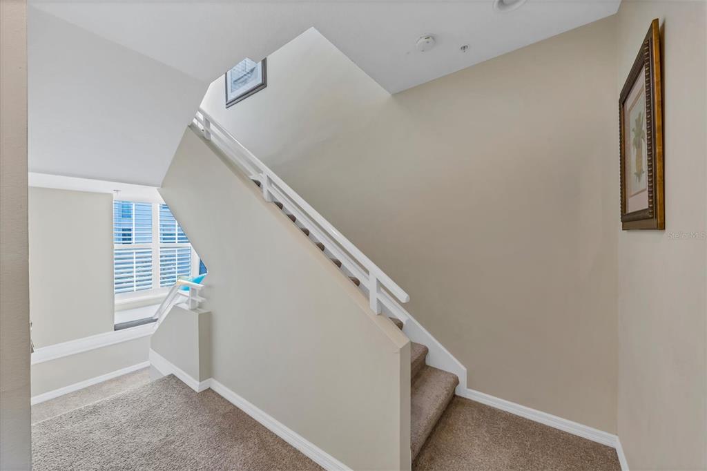 A carpeted staircase with white railings ascends along a beige wall in a residential interior — 8272 HARBORSIDE CIRCLE, ENGLEWOOD, FL
