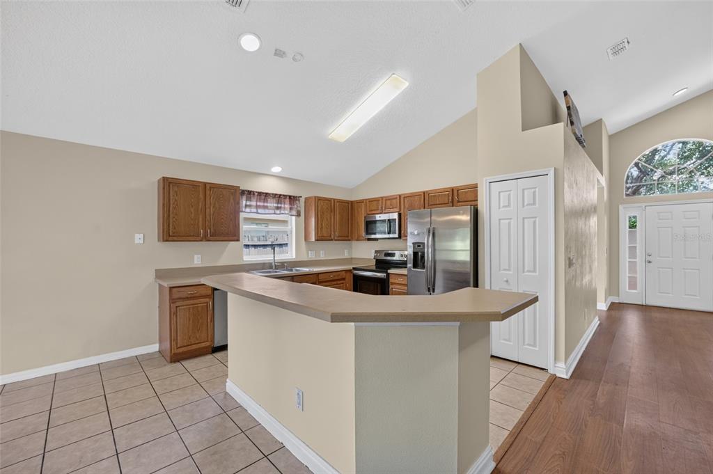A kitchen with wood cabinets, stainless steel appliances, and a breakfast bar overlooks a tiled floor — 2887 DOE RUN TRAIL, ORANGE CITY, FL