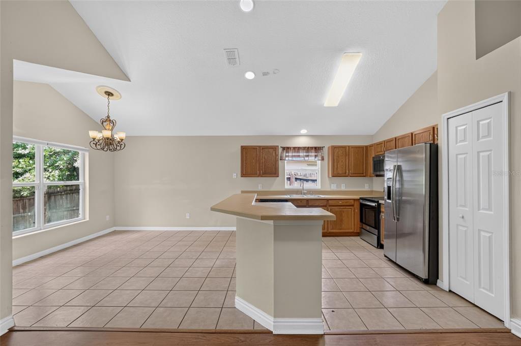 A kitchen with light-colored tile flooring, oak cabinets, stainless steel appliances, and a breakfast bar — 2887 DOE RUN TRAIL, ORANGE CITY, FL
