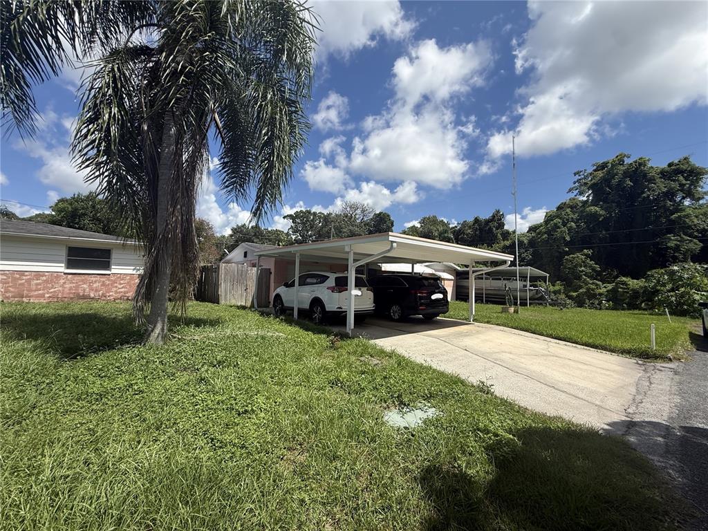 A house exterior features a carport with two parked cars and a palm tree nearby — 1650 AQUA LANE, HOLIDAY, FL