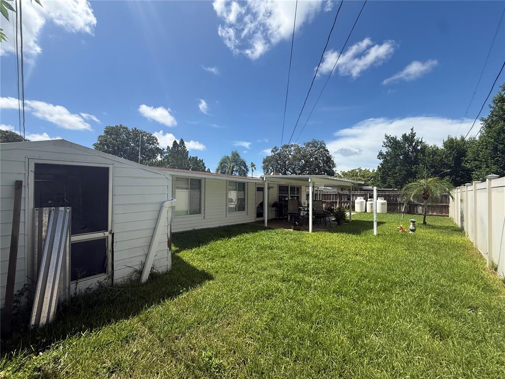 A backyard view of a white house with a shed, patio, and fenced lawn — 1650 AQUA LANE, HOLIDAY, FL