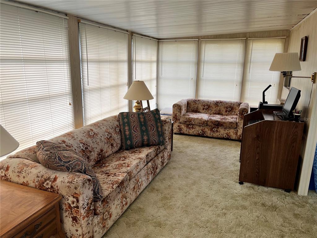A sunroom features floral sofas, beige carpeting, wood-paneled walls, and multiple windows with white blinds — 11128 102ND WAY UNIT 225, LARGO, FL