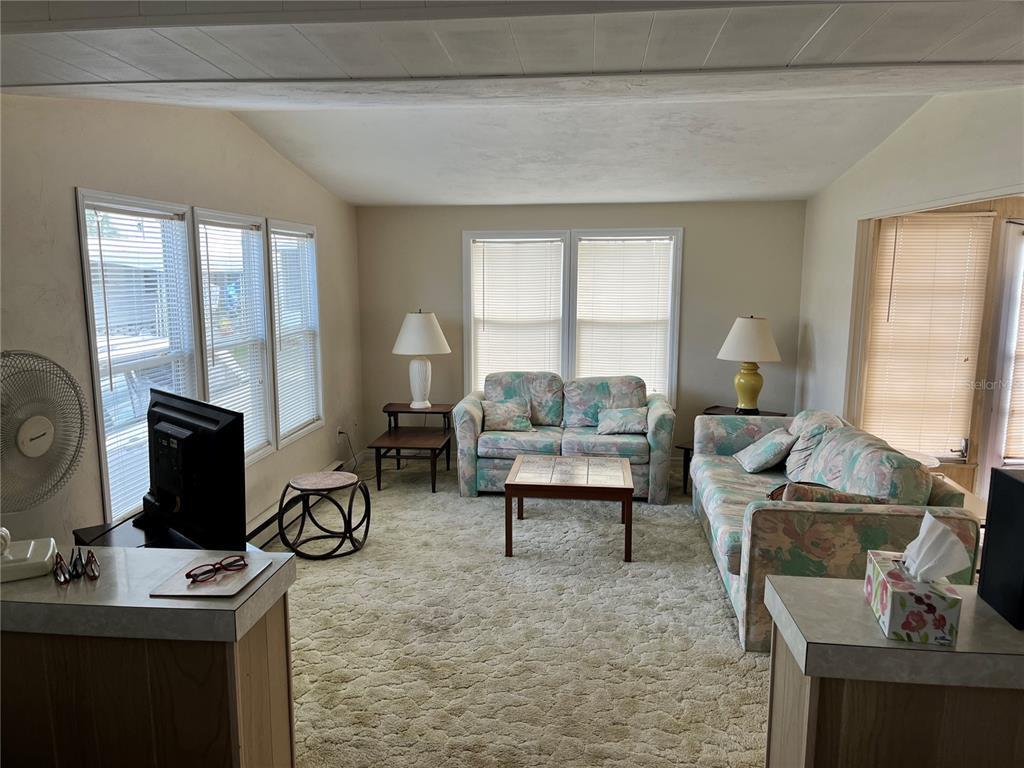 A living room features floral sofas, a coffee table, beige carpeting, and multiple windows — 11128 102ND WAY UNIT 225, LARGO, FL
