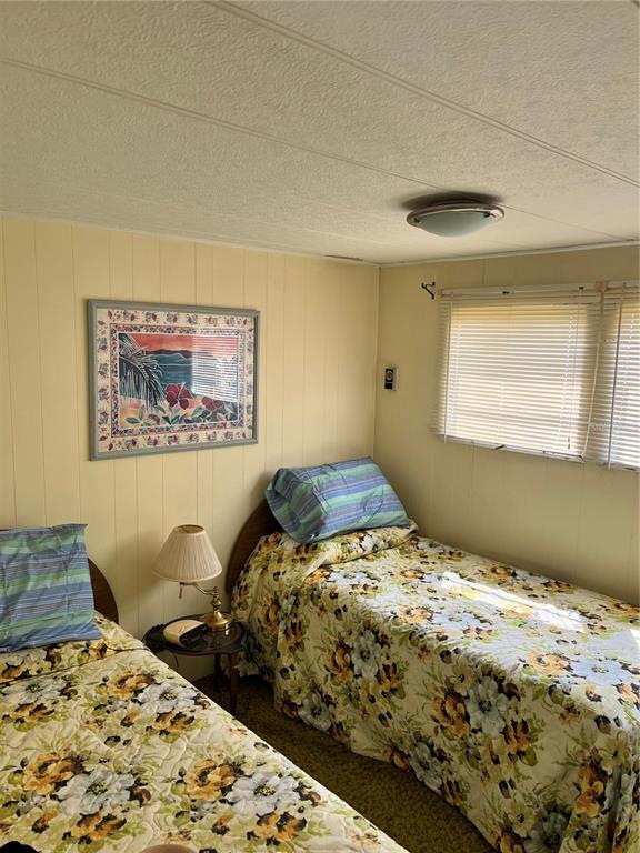 A bedroom features two twin beds with floral quilts, wood-paneled walls, and a window with blinds — 11128 102ND WAY UNIT 225, LARGO, FL