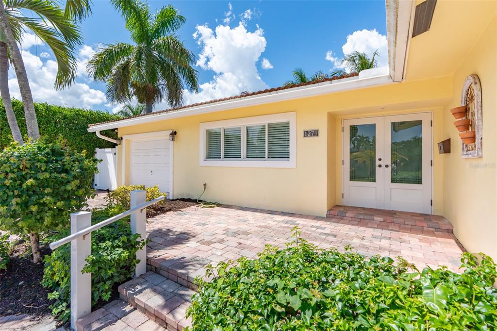 A yellow house exterior features a brick patio, double glass front doors, and palm trees — 1271 SW 9TH STREET, BOCA RATON, FL