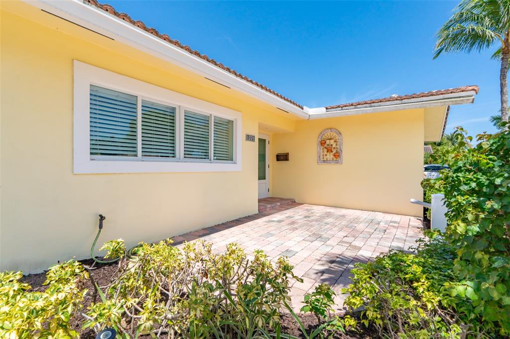 A yellow house exterior features a paved patio, a large window, and a front entrance — 1271 SW 9TH STREET, BOCA RATON, FL