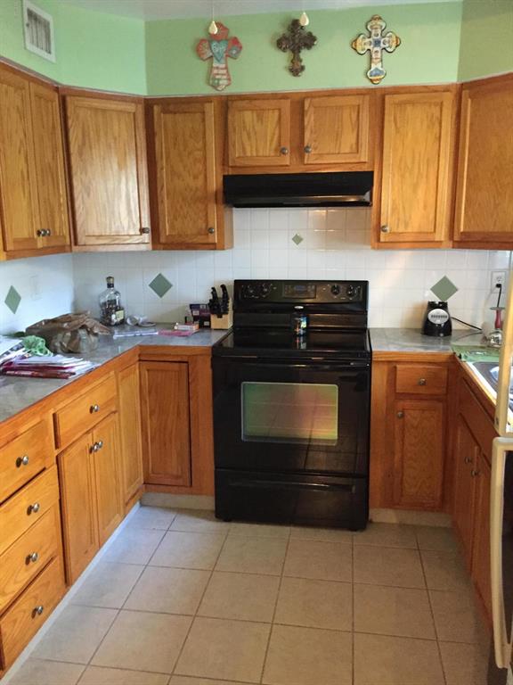 A kitchen features oak cabinets, a black stove, light countertops, and green walls with crosses — 7237 NE 33rd COURT, ANTHONY, FL