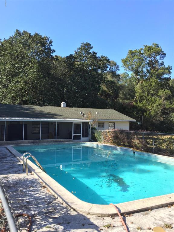 A rectangular swimming pool sits in the backyard of a house with a screened porch — 7237 NE 33rd COURT, ANTHONY, FL