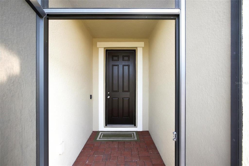 A dark brown front door is set within a covered entryway with brick flooring — 3987 RIVER BANK WAY, PORT CHARLOTTE, FL
