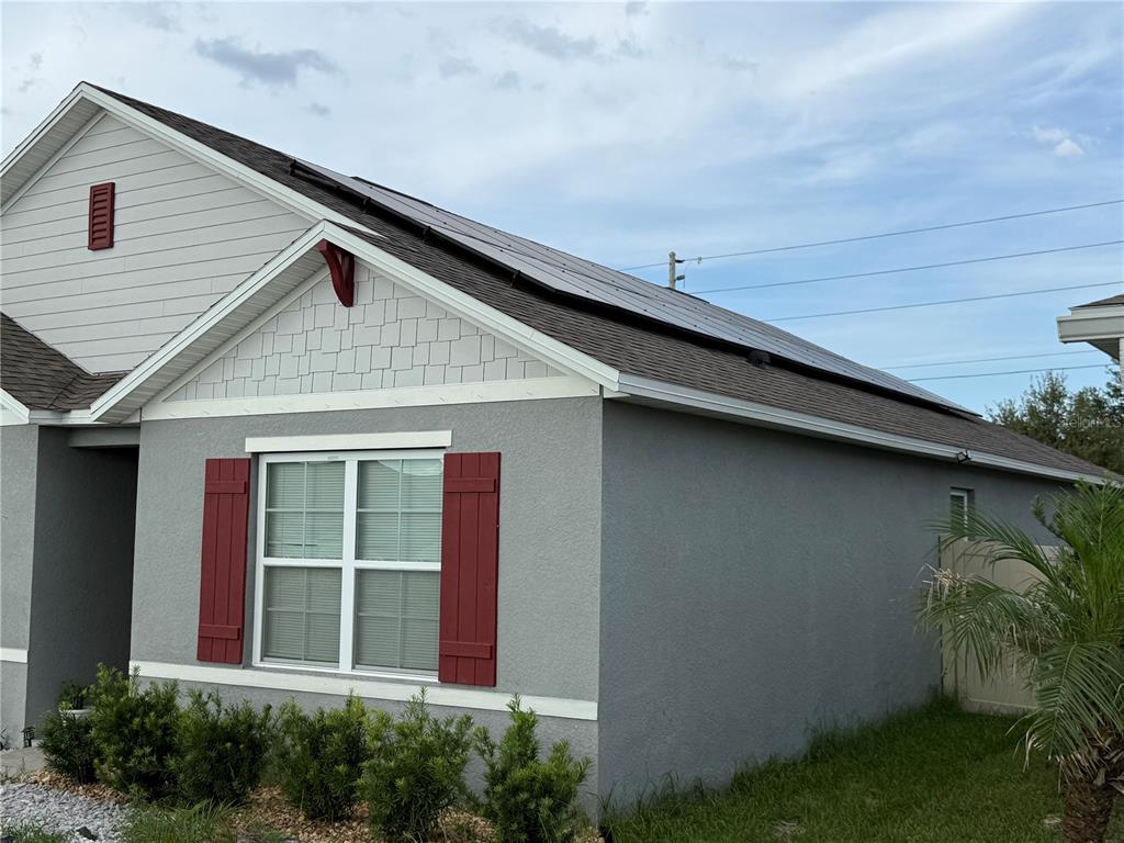 A gray house exterior features red shutters, a shingled roof with solar panels, and landscaping — 3597 YARIAN, HAINES CITY, FL