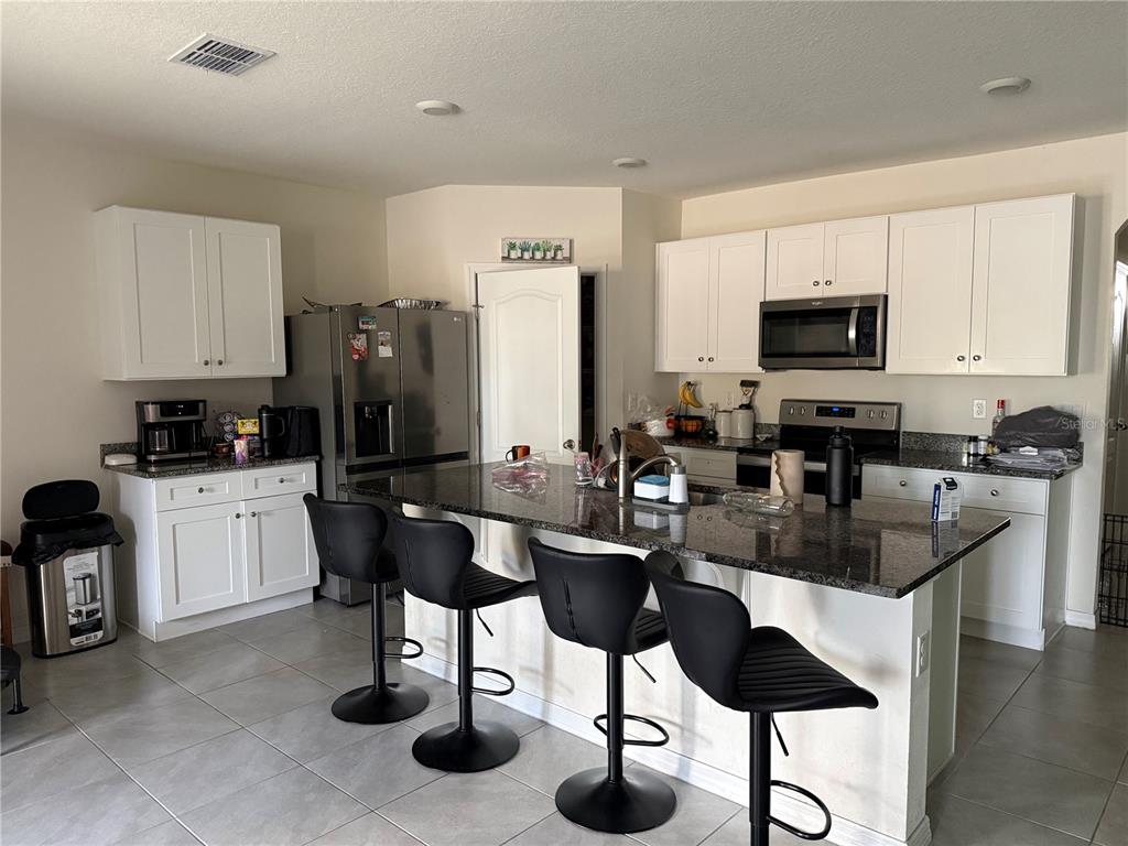 A kitchen features white cabinets, granite countertops, stainless steel appliances, and a breakfast bar with stools — 3597 YARIAN, HAINES CITY, FL