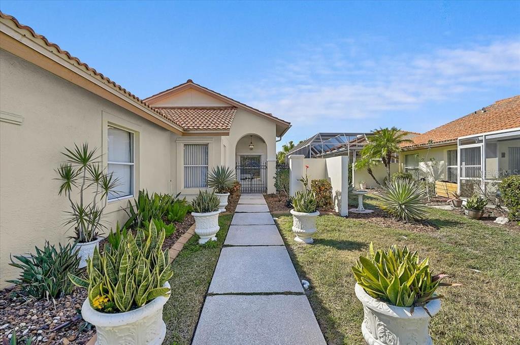 A concrete walkway leads to the gated entrance of a house with potted plants — 4640 PERIDIA BOULEVARD E, BRADENTON, FL